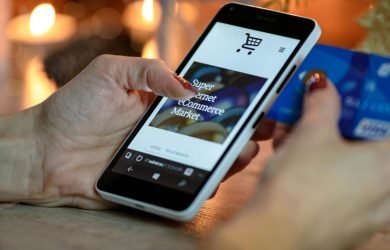 pexels-photo-230544-230544 Woman using smartphone for online shopping with credit card in hand, festive background lighting.